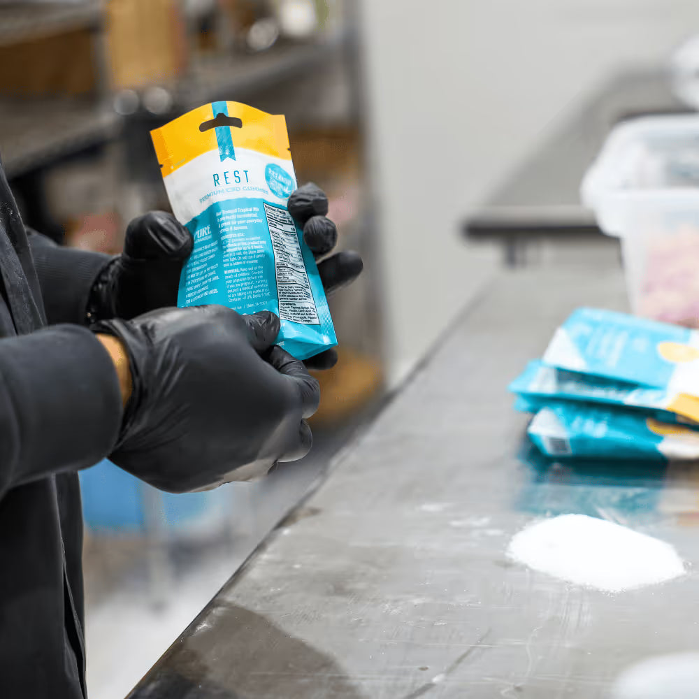 Gloved production worker holding a sealed THC gummy package