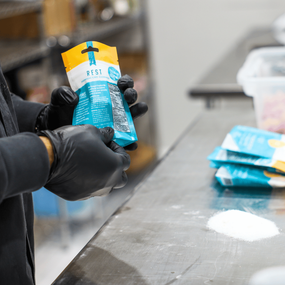 Gloved production worker inspecting a sealed gummy package