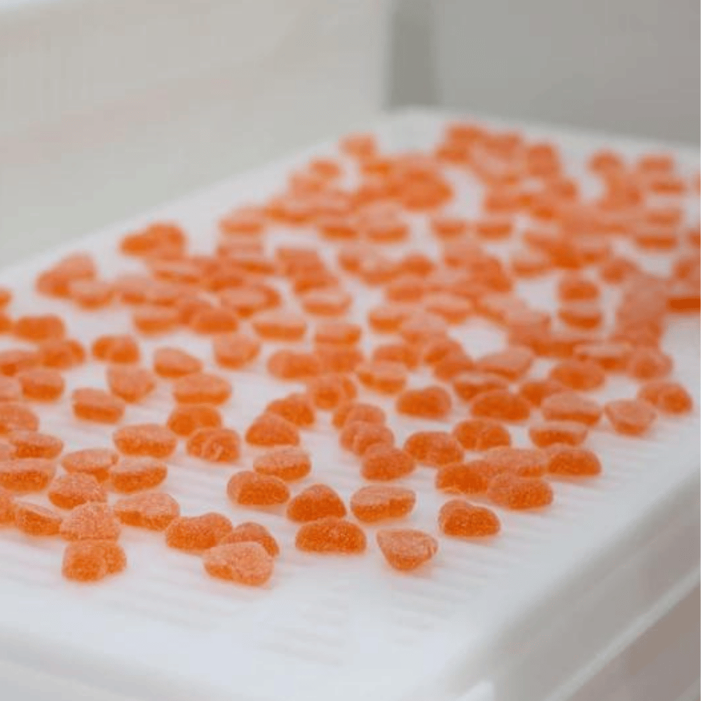 Orange sugar-coated gummies arranged on a production tray