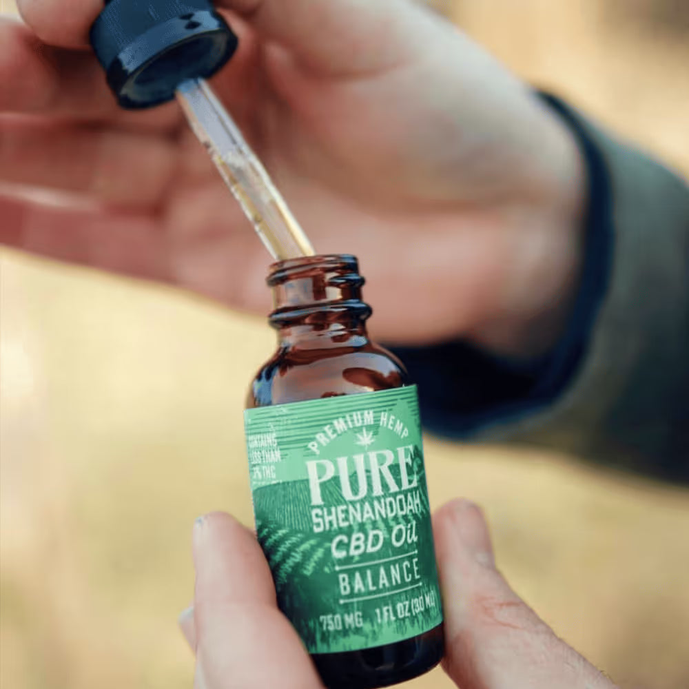 Dropper dispensing Calm CBD oil above a Pure Shenandoah bottle