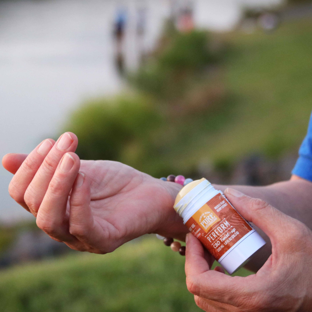 Person applying Pure Shenandoah Perform CBD Twist-up, 2000 mg topical stick, to wrist outdoors for daily use.